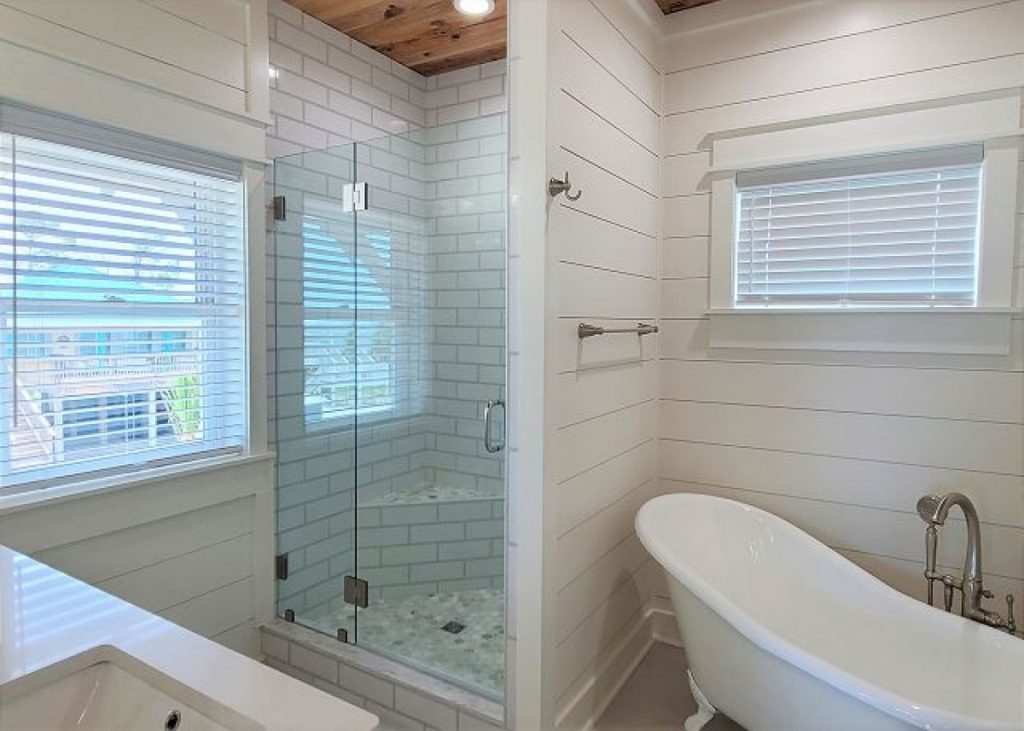 Bathroom with subway tile shower stall and fancy standalone tub, two windows.